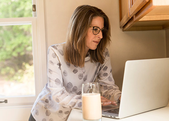 Woman standing at counter looking at laptop with glass of milk