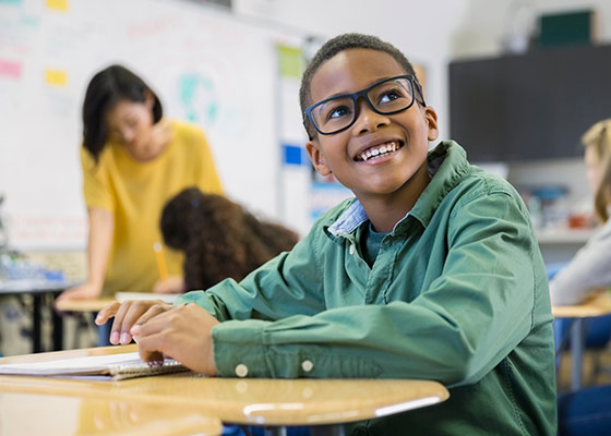 young boy with olive green shirt and glasses looking up at a teacher with a smile