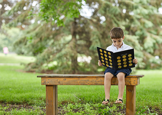 boy sitting outside on a bench looking at a yearbook